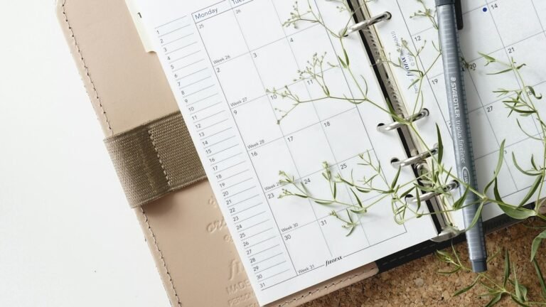 Open paper planner with a pen and green sprigs on the pages.