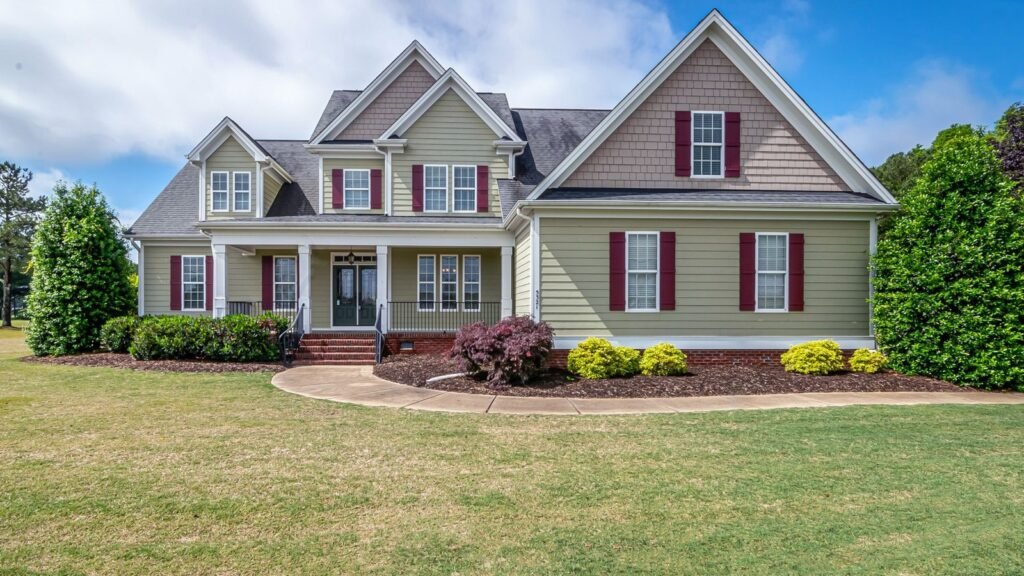 A two-story suburban house with a covered porch, front lawn and shrubs.