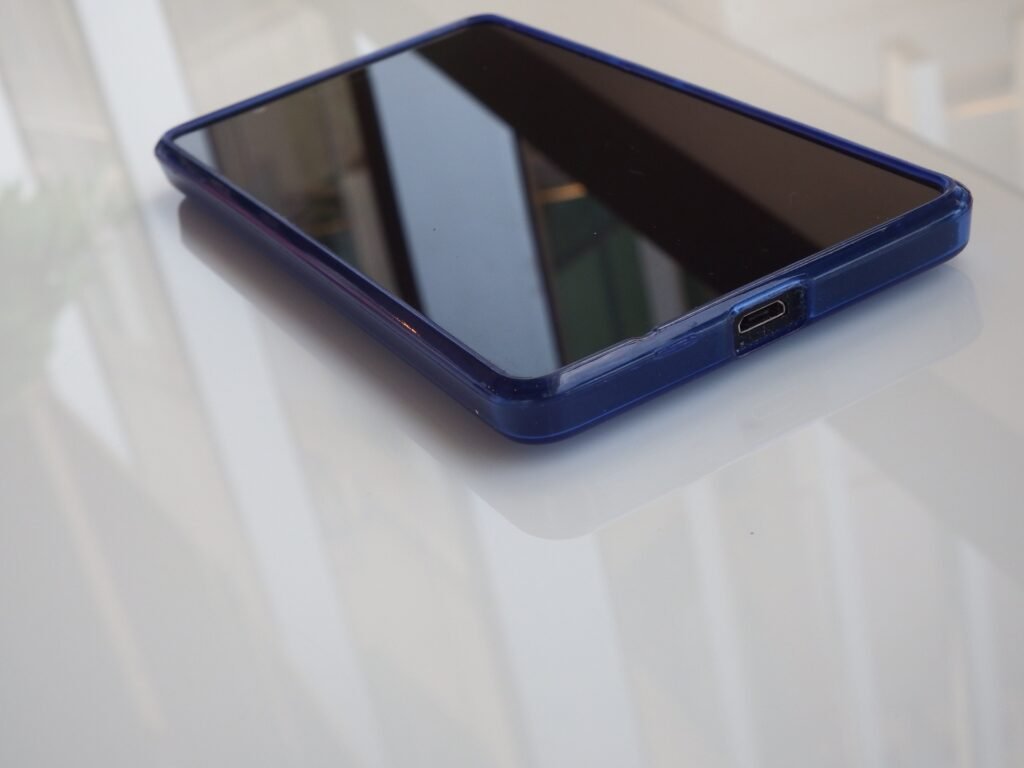 A smartphone in a blue case rests on a light reflective surface with its screen blank.