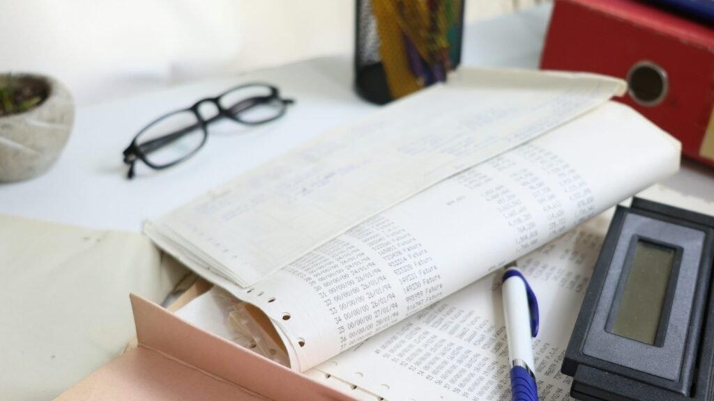 Printed accounting records, a calculator, a pen and eyeglasses on a desk.