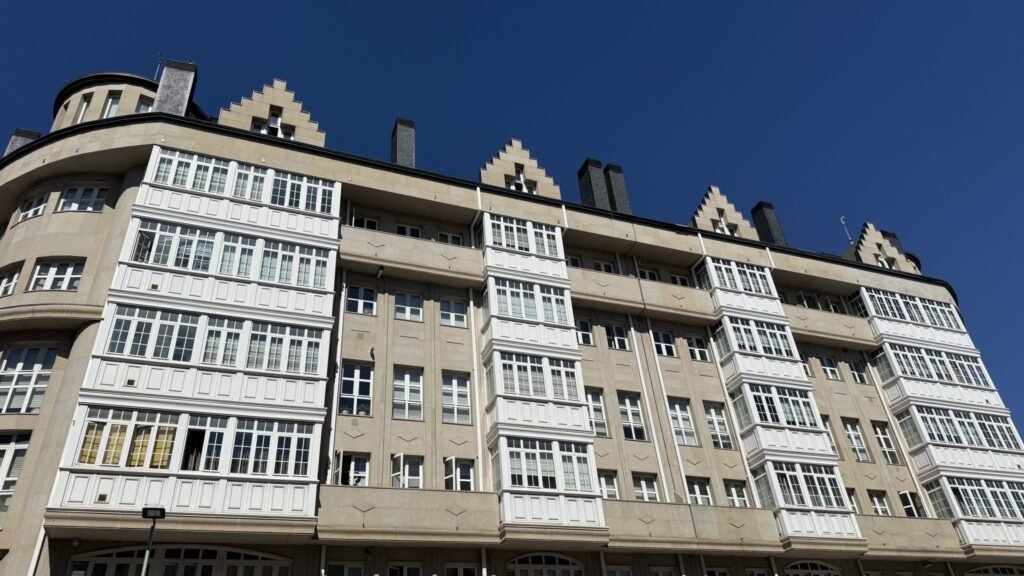 A beige multi-story building with white enclosed balconies beneath a blue sky.