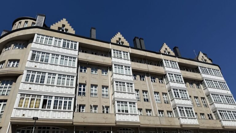 A beige multi-story building with white enclosed balconies beneath a blue sky.