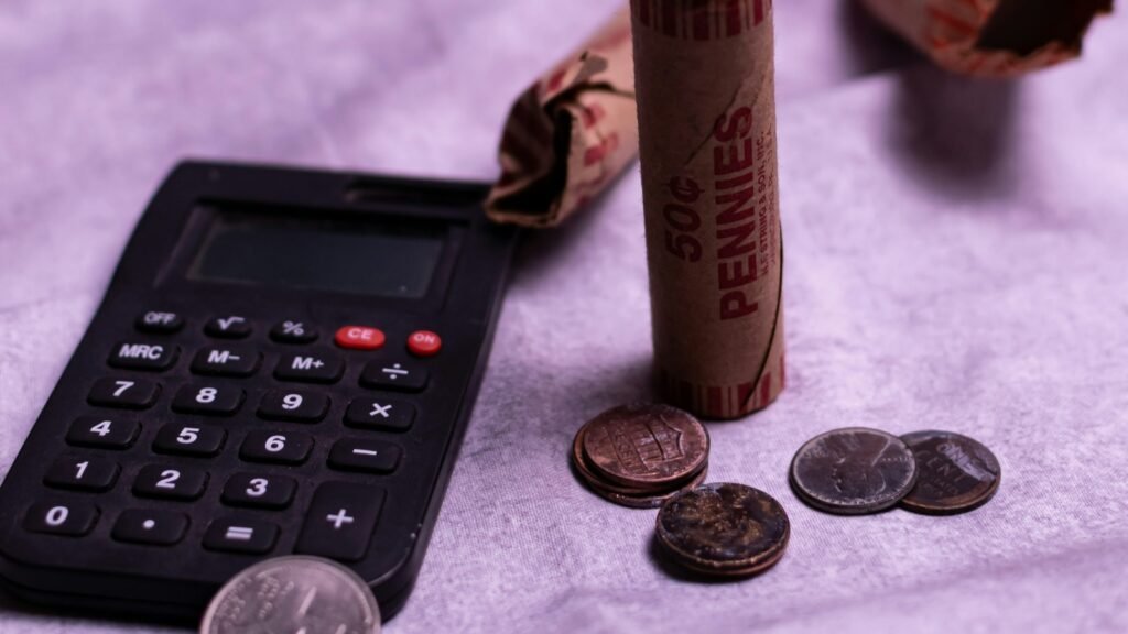 Black calculator, paper coin wrappers and loose coins on a fabric surface.