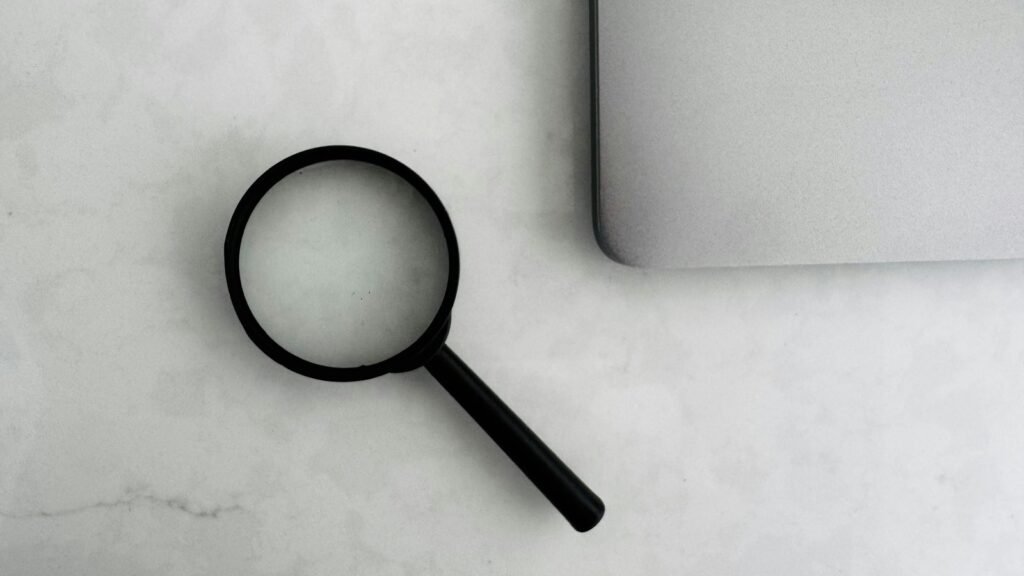 A black magnifying glass beside the corner of a closed silver laptop.