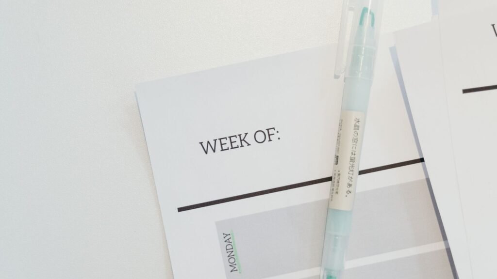 A pale pen rests diagonally on an open weekly planner.