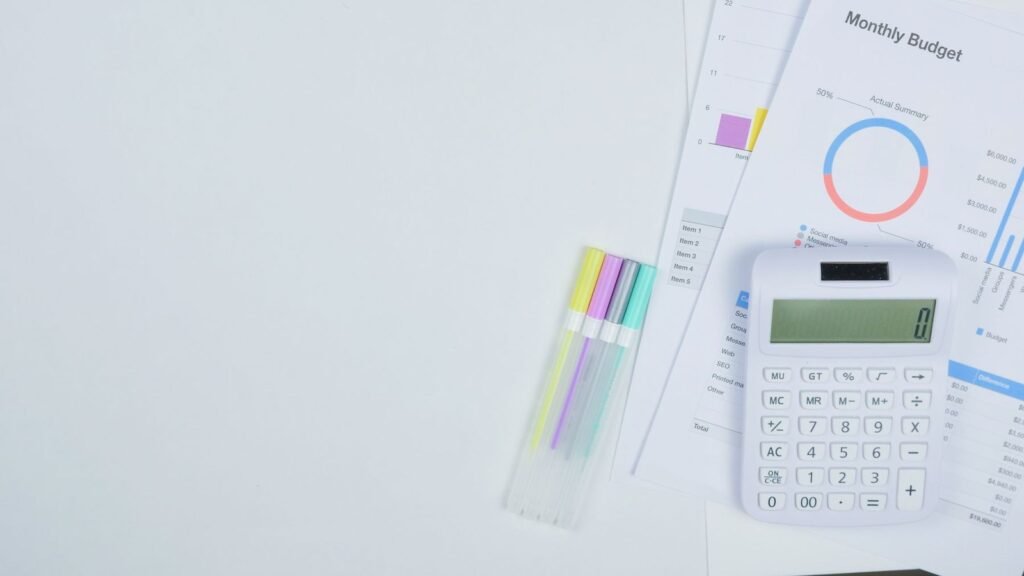 White calculator and colored pens beside a monthly budget worksheet.