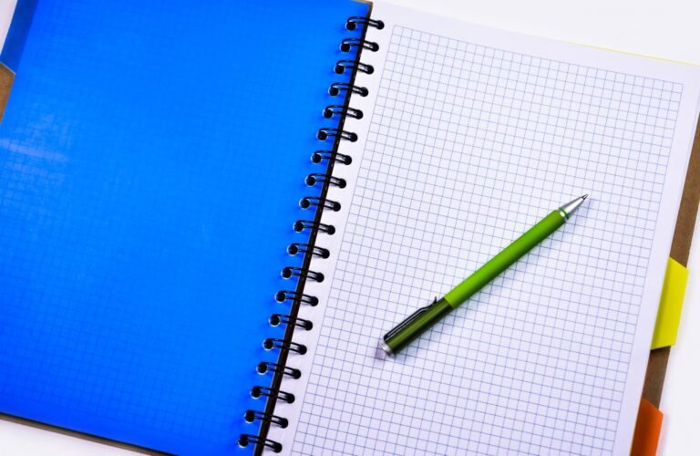 Green pen on a blank squared notebook beside a blue cover.