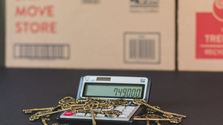 Brass-colored keys rest on a calculator in front of moving boxes.