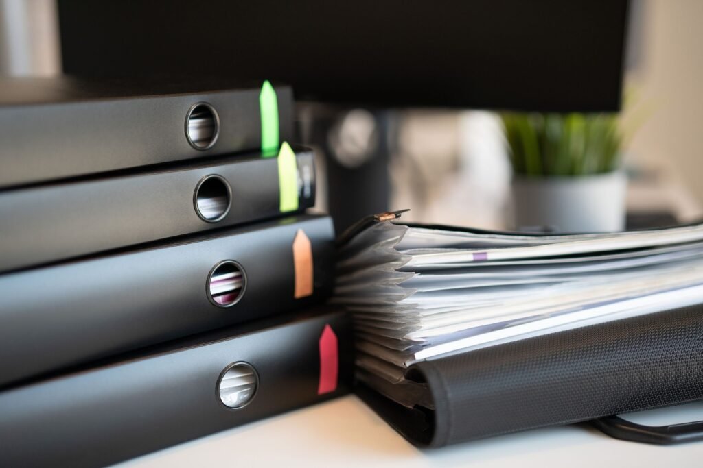 Black ring binders with colored tabs sit beside an expanding file filled with papers.