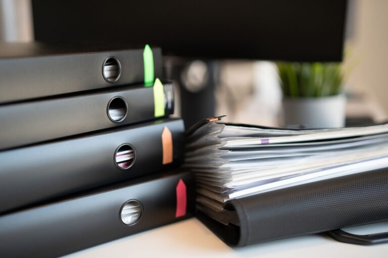 Black ring binders with colored tabs sit beside an expanding file filled with papers.