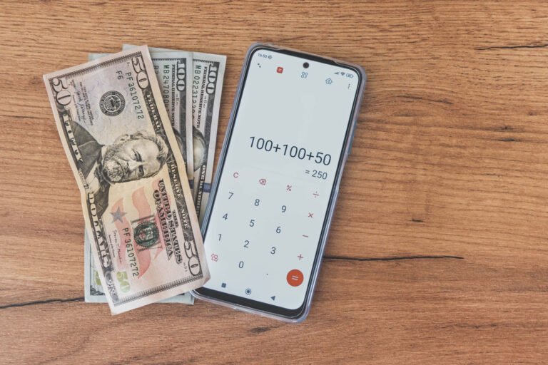 U.S. banknotes beside a smartphone displaying a calculator on a wooden surface.