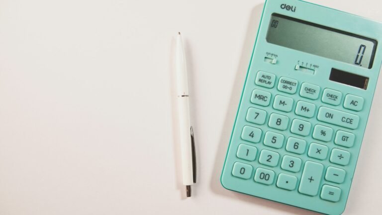 Teal calculator and a white pen on a pale surface.