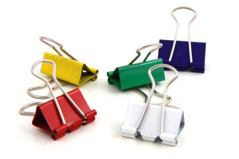 Red, yellow, green, blue and white binder clips on a white surface.