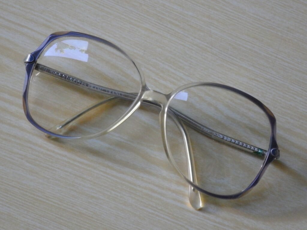 A pair of reading glasses resting on a light wood-patterned surface.