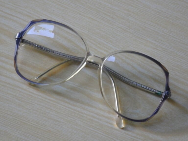 A pair of reading glasses resting on a light wood-patterned surface.