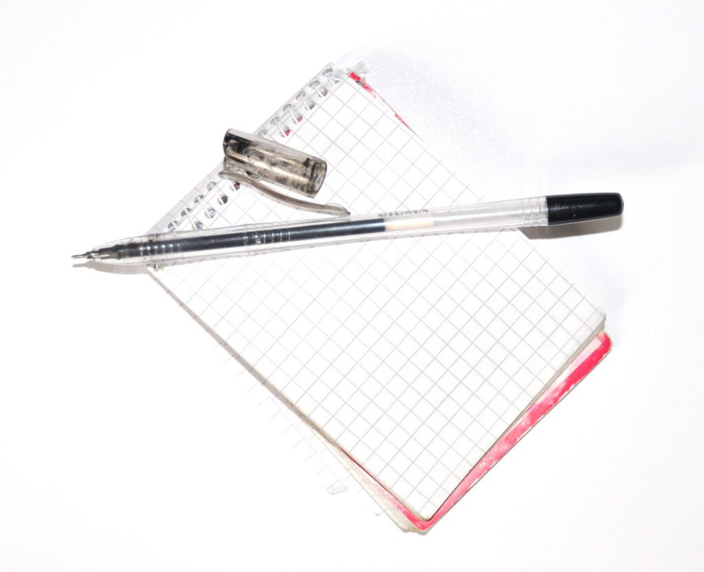 A transparent pen and its cap resting on a blank squared spiral notebook.