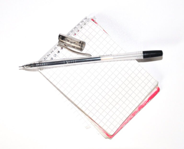 A transparent pen and its cap resting on a blank squared spiral notebook.