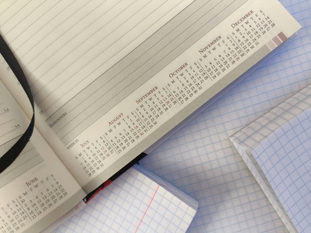 An open planner with printed monthly calendars rests on blank squared notebooks.