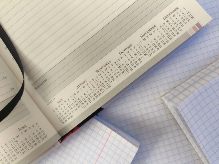 An open planner with printed monthly calendars rests on blank squared notebooks.