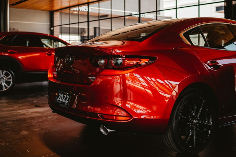 The rear of a red sedan beside another red vehicle in a showroom.