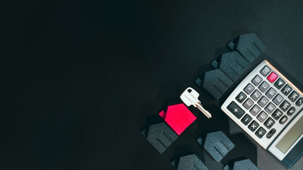 A silver key, a red model house, dark model houses and a calculator on a black surface.
