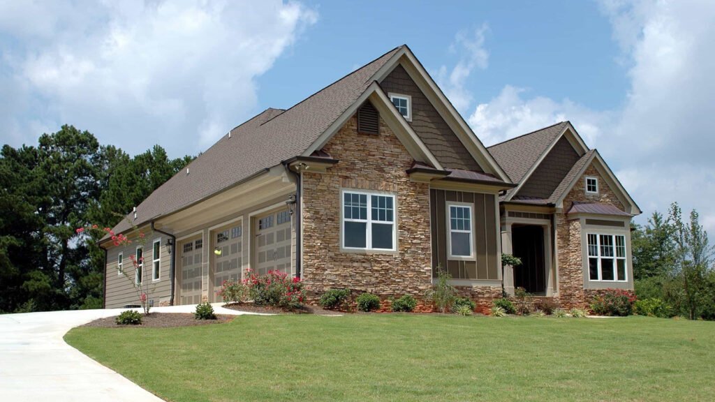 A house with a stone facade, attached garage, front lawn and curved driveway.