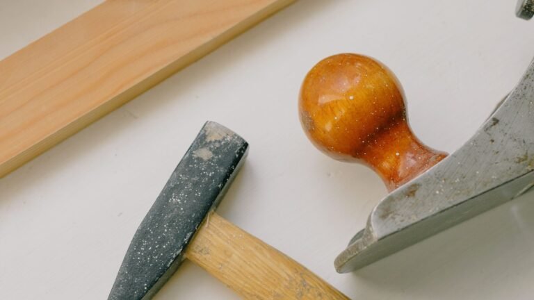 A hammer and metal hand plane rest beside a wood strip on a white surface.