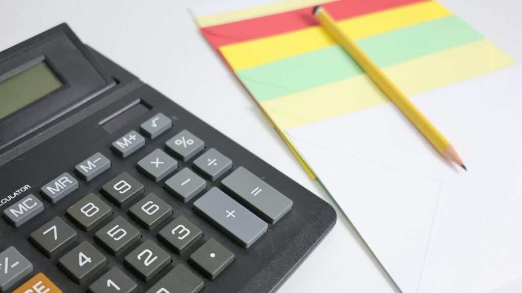Black calculator, yellow pencil and colorful stationery on a white surface.
