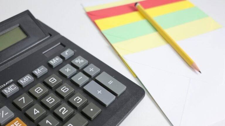 Black calculator, yellow pencil and colorful stationery on a white surface.