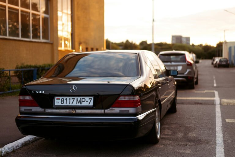 A dark sedan is parked beside a yellow building, with other cars farther along the road.