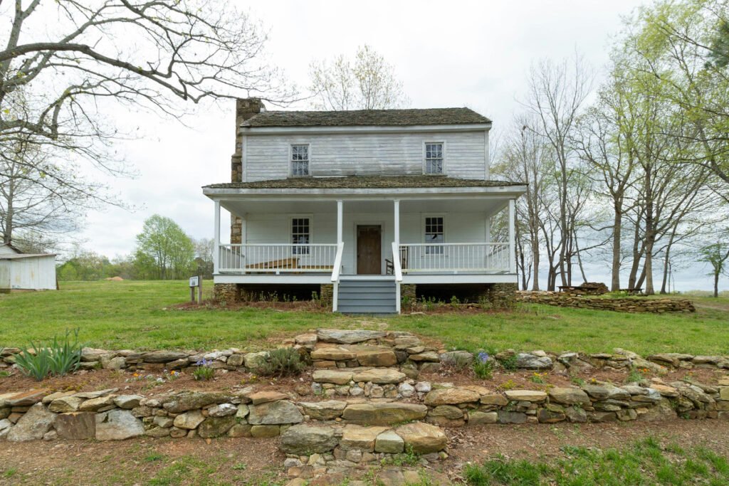 A white two-story country house with a front porch, stone steps and surrounding trees.