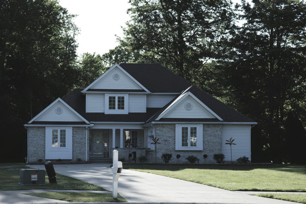 A detached house with pale siding, a dark roof, lawn and trees.
