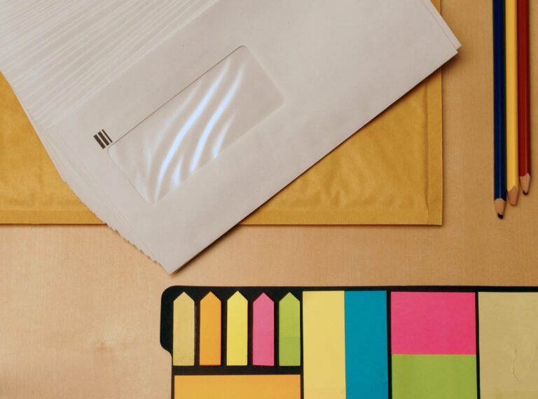 Blank window envelopes, colored pencils and sticky notes on a wooden desk.