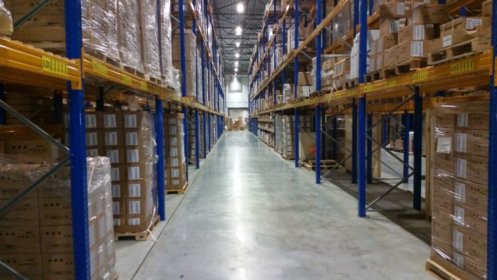A clear warehouse aisle between tall blue-and-yellow racks filled with cardboard cartons.