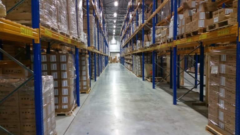 A clear warehouse aisle between tall blue-and-yellow racks filled with cardboard cartons.