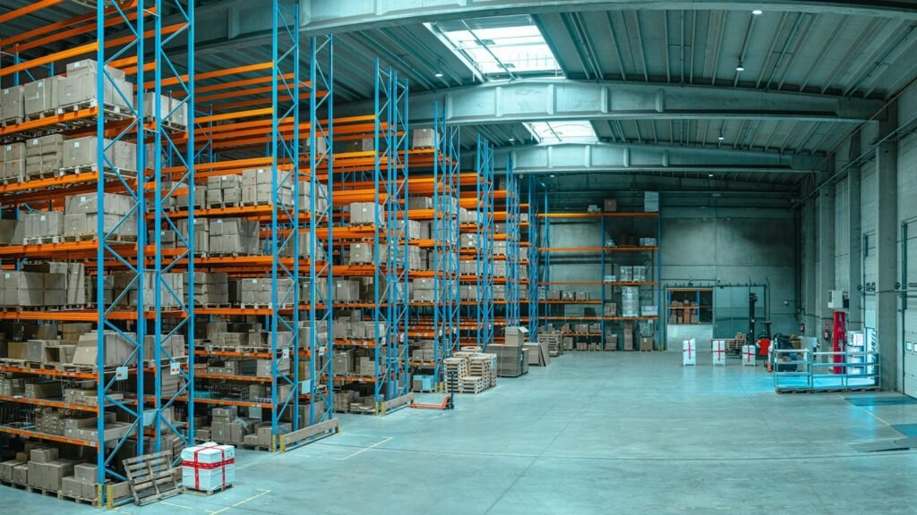 Warehouse racks hold pallets of boxes beside loading doors.