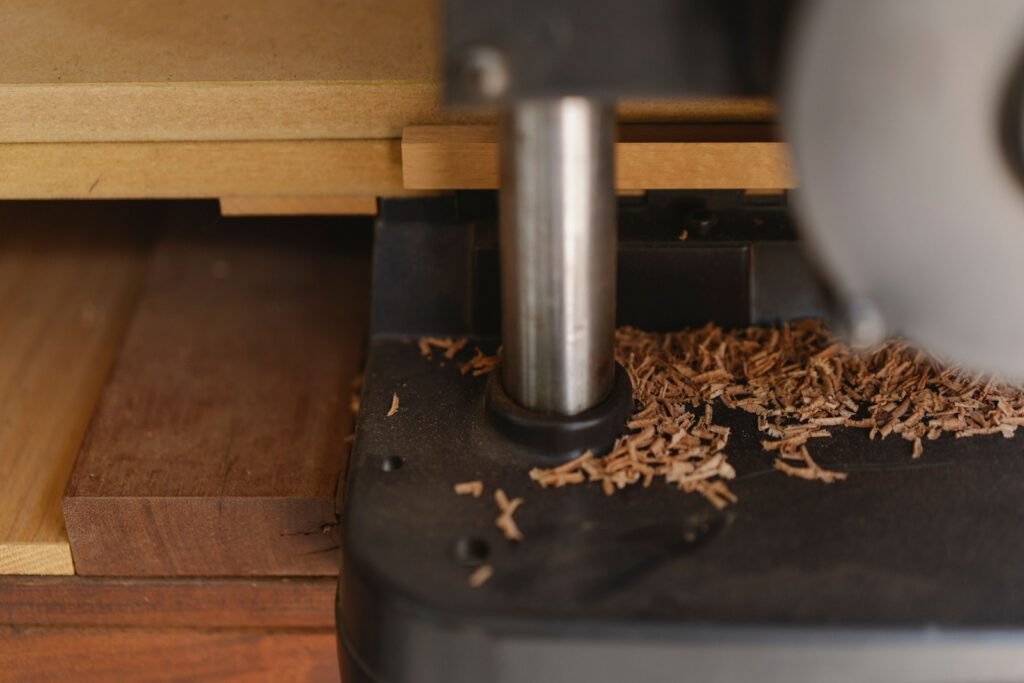 Close-up of a woodworking machine beside stacked timber, with wood shavings on its dark metal base.