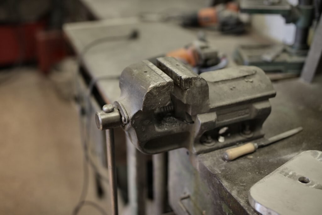 A metal bench vise beside a hand file, with power tools blurred in the background.